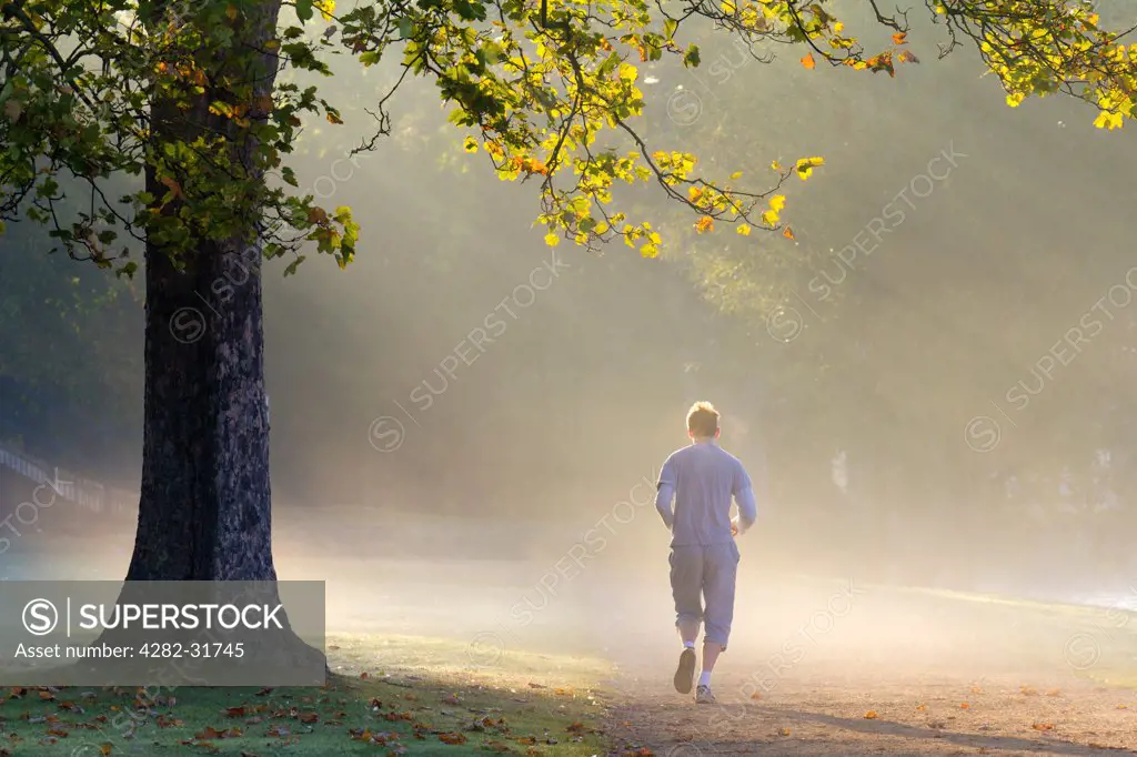 England, Oxfordshire, Christ Church. A solitary jogger running on a misty autumn morning by the river Thames at Oxford.