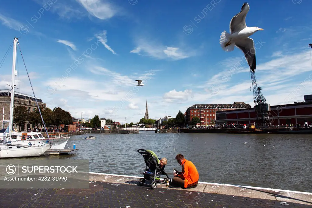 England, Bristol, Harbourside. A father and child sit beside the River Avon at Harbourside in Bristol.