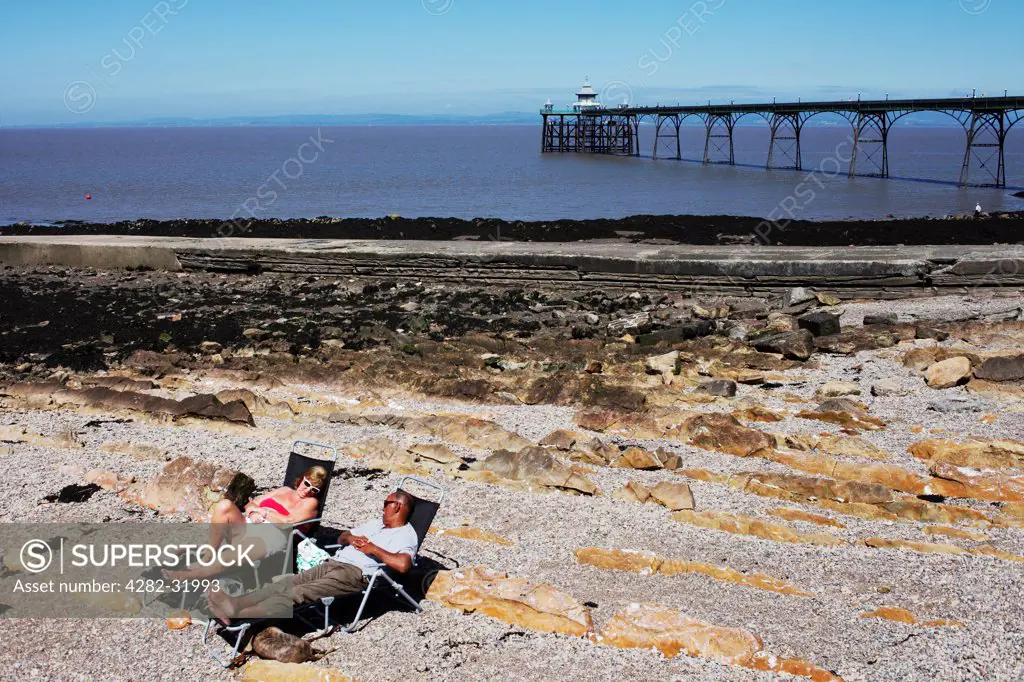 England, Bristol, Cleveden. Two people lay on recliners on the beach at Cleveden.