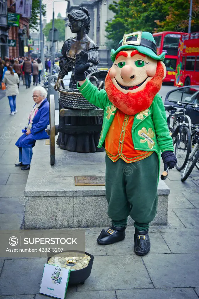 Ireland, Dublin, Dublin. A street performer dressed as a leprechaun next to a statue of Molly Malone in Grafton Street.