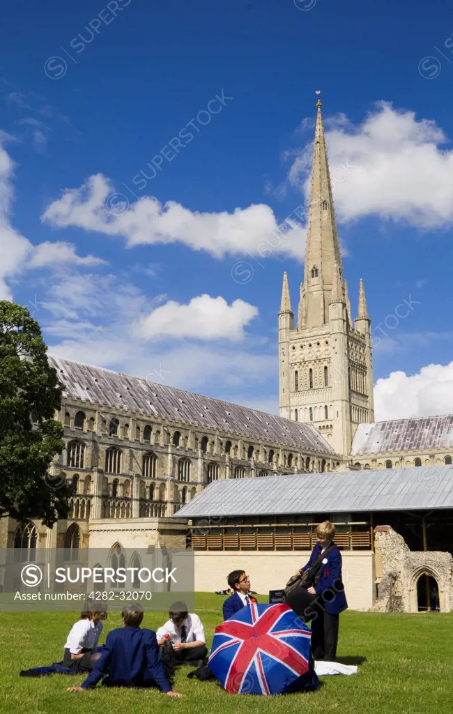 England, Norfolk, Norwich. Pupils from Norwich School relax on the grass in front of Norwich Cathedral.