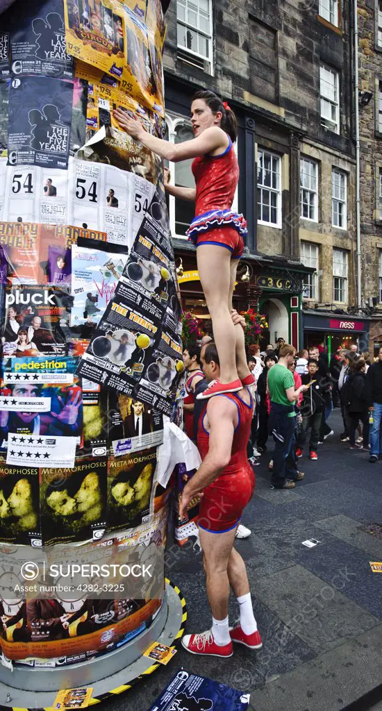 Scotland, City of Edinburgh, Edinburgh. Performers sticking a poster to a column in the High Street advertising shows on at the Fringe at the Edinburgh Festival.