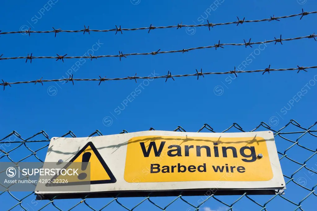 England, North Yorkshire, York. Warning sign on a barbed wire fence against bright blue sky.