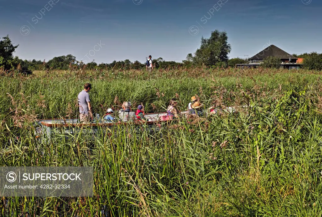 England, Cambridgeshire, Wicken. Tourists on a boat travelling through the canals of Wicken Fen in Cambridgeshire in Summer.