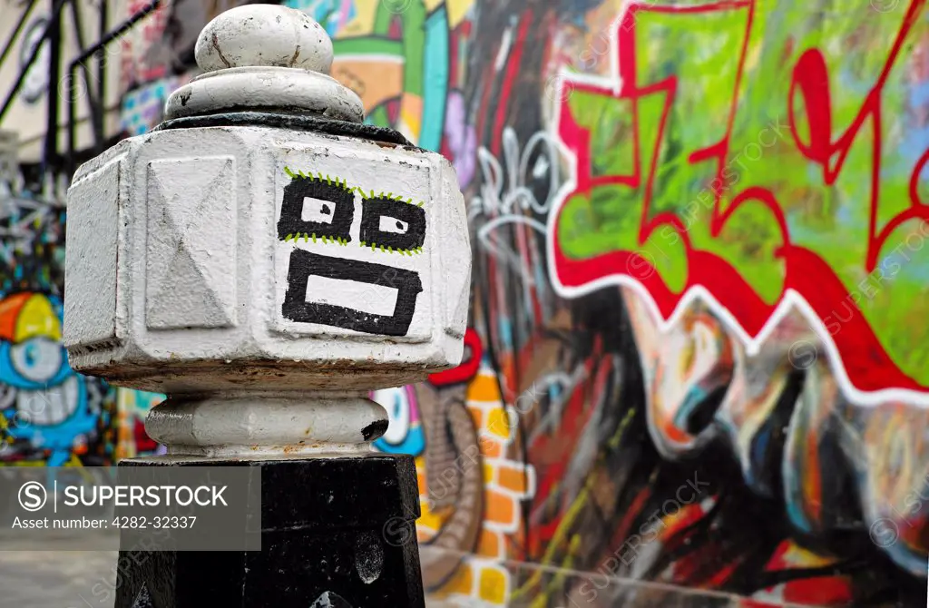 England, London, Brick Lane. Brick Lane bollard face with graffiti behind.