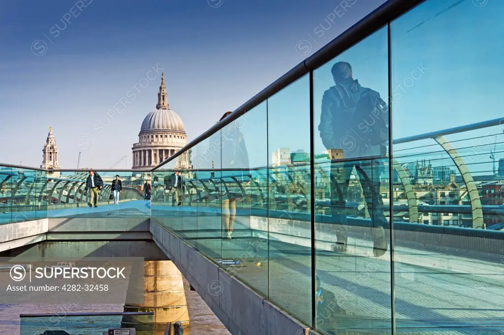 England, London, Millenium Bridge. View of St Paul's Cathedral through glass railings of the Millenium bridge with pedestrians.