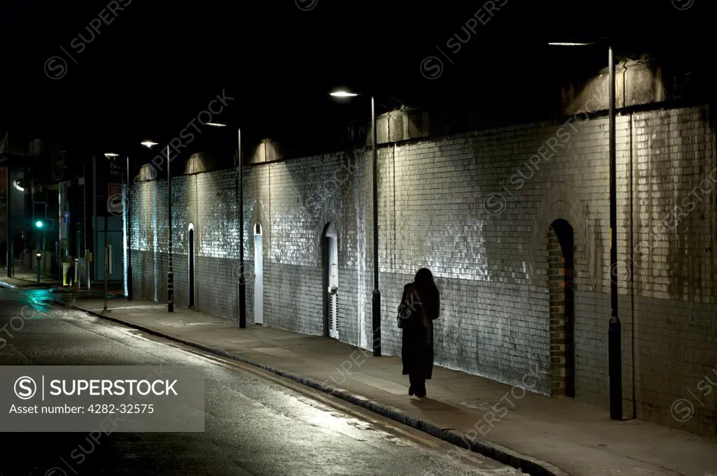 England, Greater Manchester, Manchester. A woman walks alone beneath a dark tunnel in Manchester.