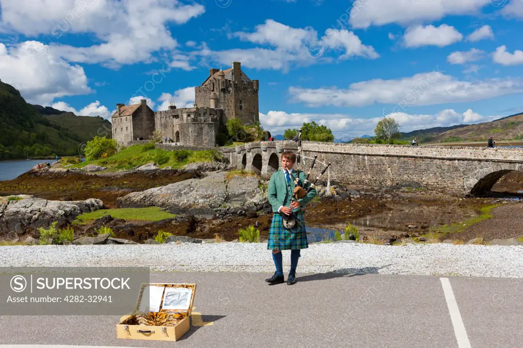 Scotland, Highland, Dornie. A lone piper plays in front of Eilean Donan castle and Loch Duich.