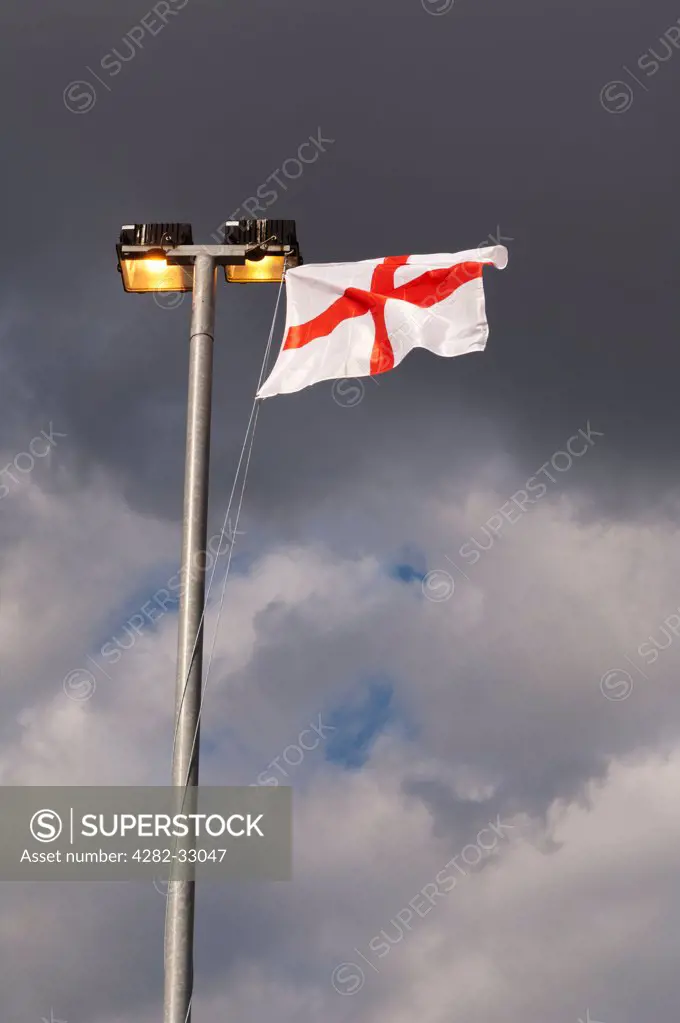 England, London, Greenwich. The England flag waving in the wind from the top of a set of floodlights in an industrial yard in Greenwich.