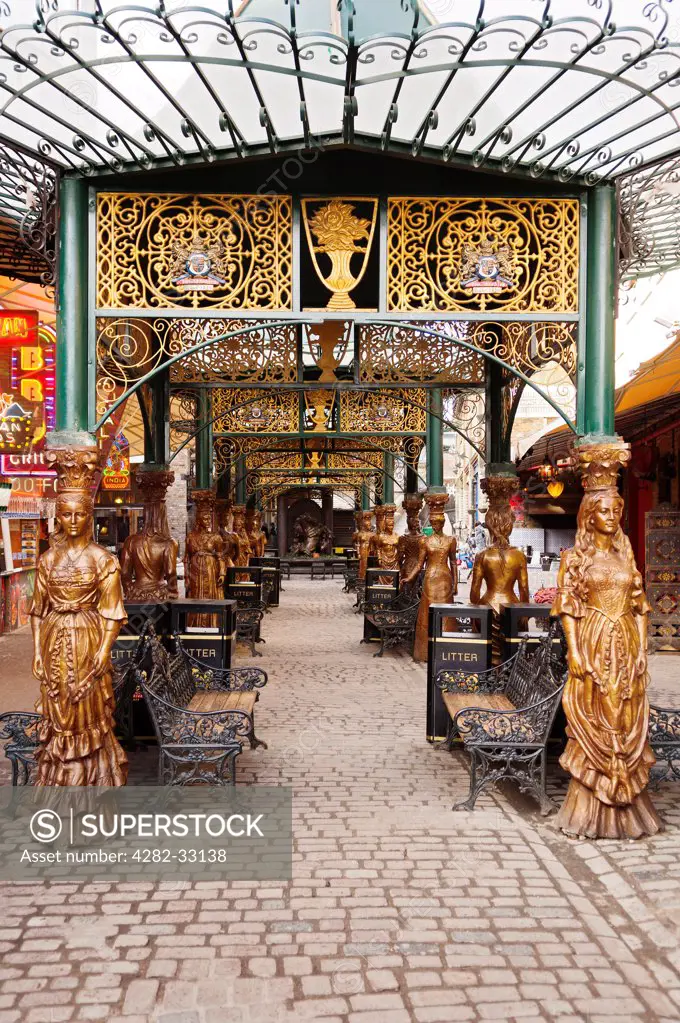 England, London, Camden. Covered walkway lined with benches and gilded statues in The Stables Market in Camden.