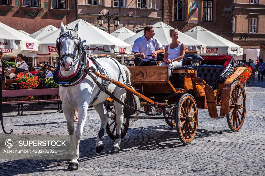 Poland, Mazovia Province, Warsaw. A young woman tourist takes a ride in a horse and carriage in Stary Rynek in Warsaw.