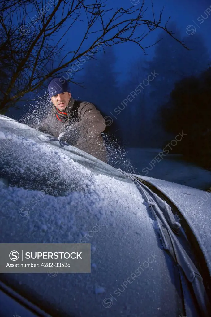Wales, Monmouthshire, Monmouth. Man scraping ice from a frost covered car windscreen.