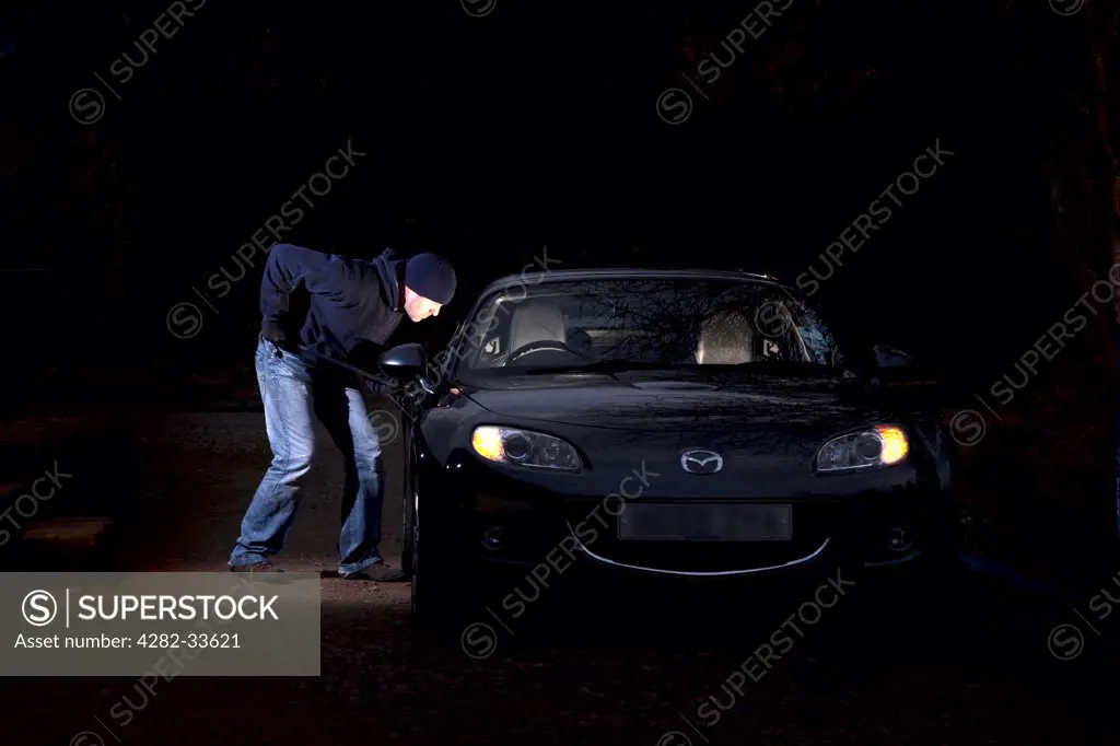 Wales, Monmouthshire, Monmouth. A man breaking into a parked car at night.