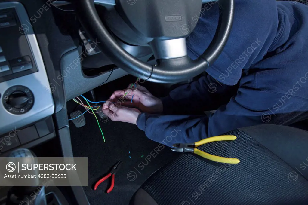 Wales, Monmouthshire, Monmouth. A man wearing a hoody hot wiring a car.