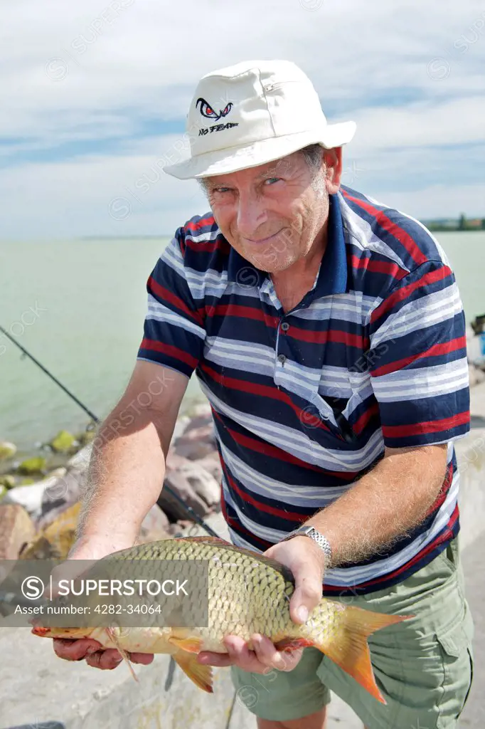 Hungary, Somogy, Balatonszemes. A fisherman with his catch on the breakwater of the Balatonszemes marina at Lake Balaton.