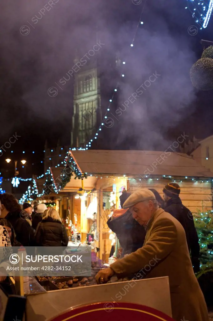 England, Gloucestershire, Cirencester. A stall holder selling roasted chestnuts at a Christmas Market in the Cotswolds.