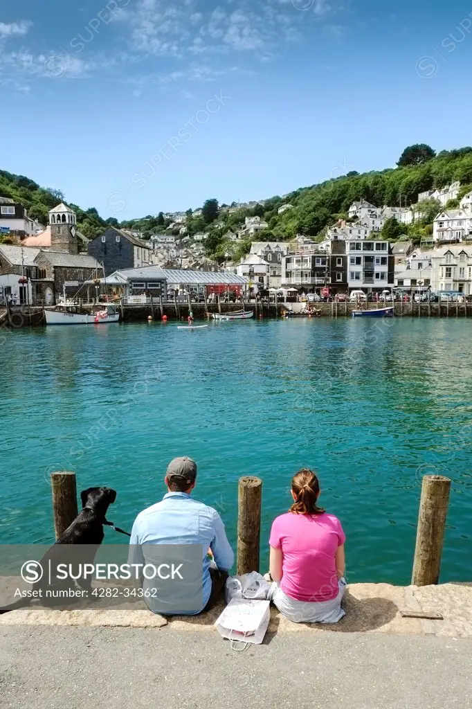England, Cornwall, Looe. A couple and their dog sitting on the quayside in Looe.