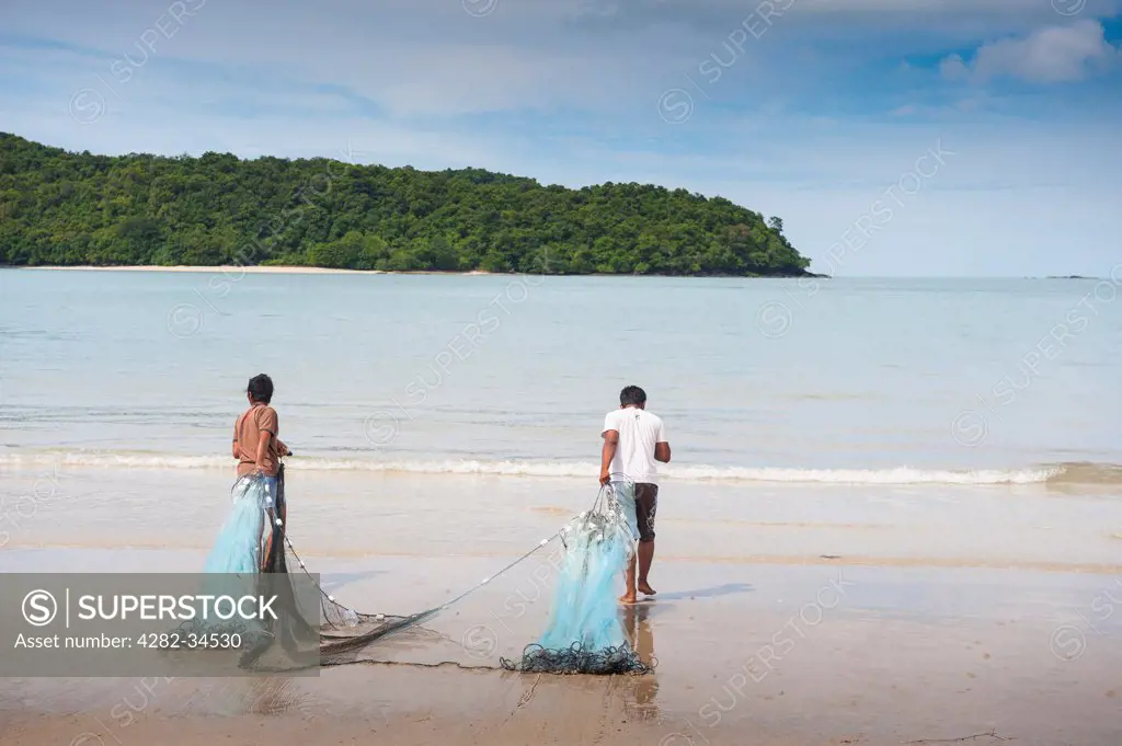 Malaysia, Kedah, Langkawi Permata Kedah. Two Malaysian fishermen dragging a fishing net across Pantai Tengah beach in Langkawi.