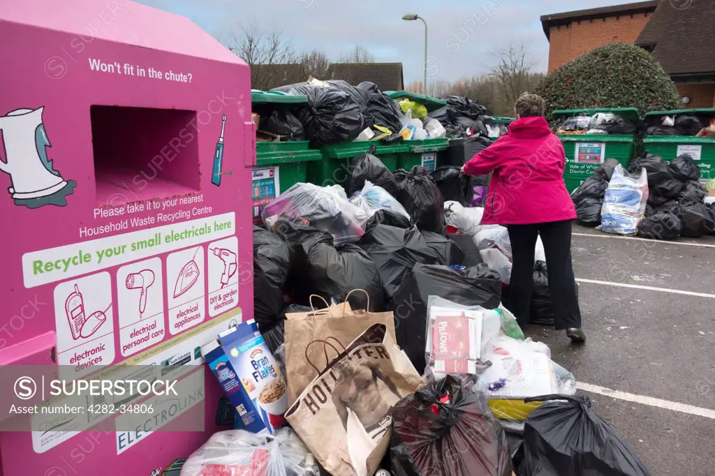 England, Oxfordshire, Abingdon. Woman discarding garbage at an overflowing waste recycling point at Peachcroft Housing Estate in Abingdon.