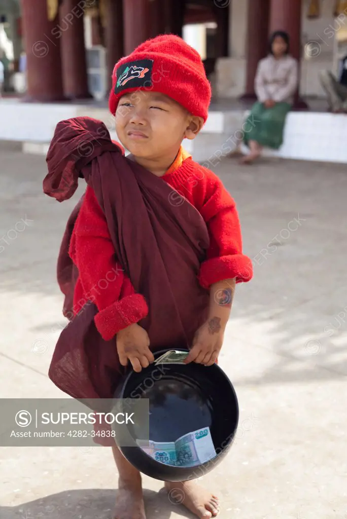 Myanmar, Mandalay, Bagan. A tiny boy in Monk's robes and red hat with a his collection bowl in Shwezigon Pagoda in Bagan in Myanmar.