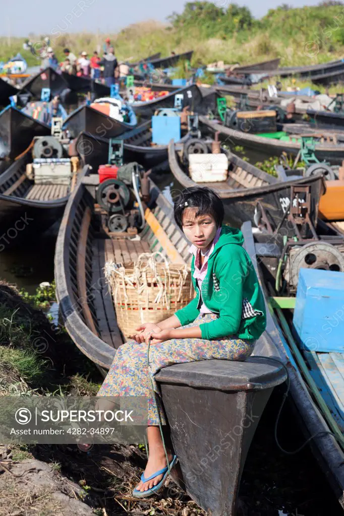 Myanmar, Shan, Lake Inle. A young girl sitting by moored boats in a small village by Lake Inle in Myanmar.
