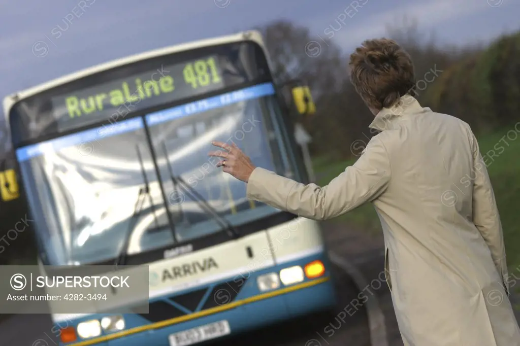 England, Shropshire, Telford. Woman hailing a bus to stop on a rural bus route. Telford is named after Thomas Telford, a famous civil engineer.
