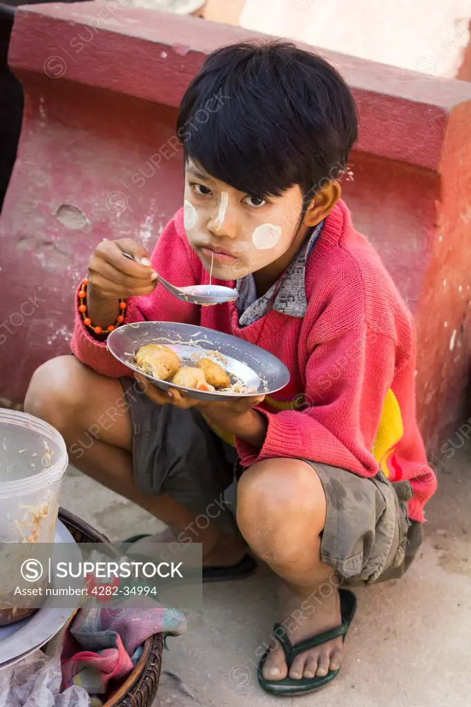 Myanmar, Mandalay, Mingun. A young boy eats lunch in Mingun in Myanmar.