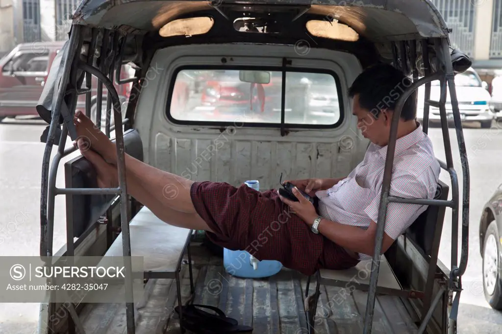 Myanmar, Yangon, Yangon. A driver texting in the back of his public transport pickup in Yangon in Myanmar.