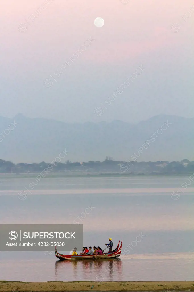 Myanmar, Mandalay, Lake Taungthaman. A full moon above Taungthaman Lake in Myanmar and late tourist boat going home.