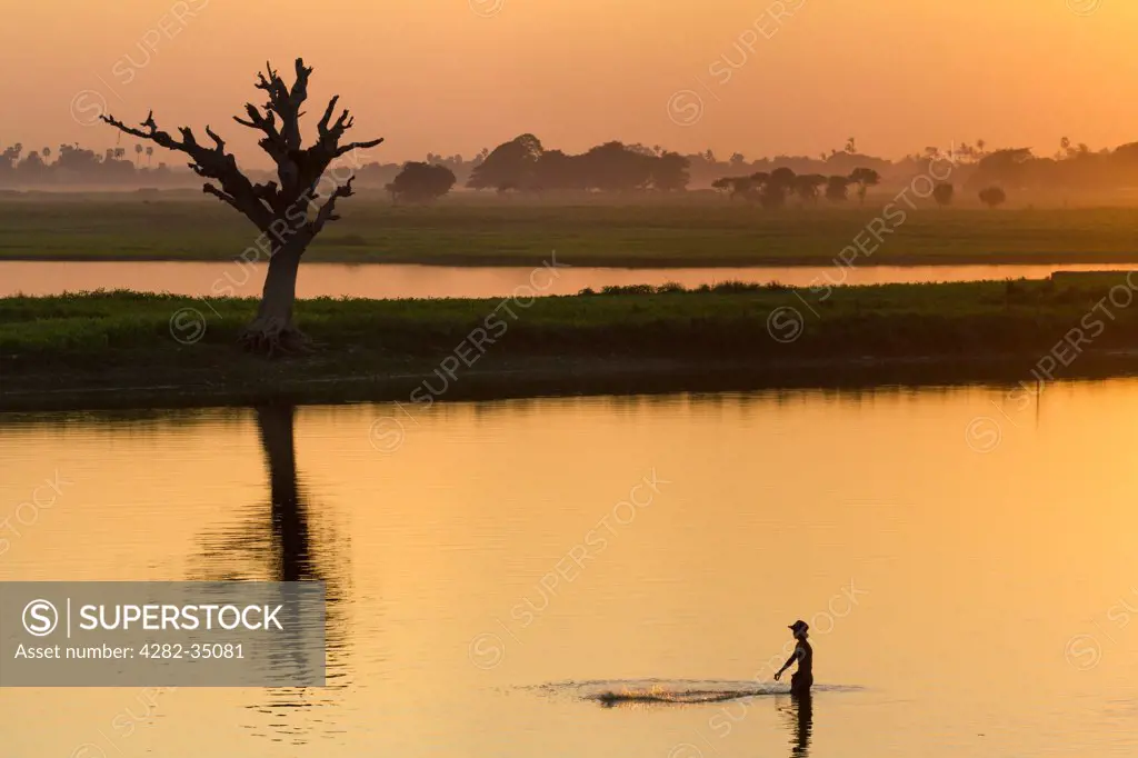 Myanmar, Mandalay, Lake Taungthaman. A fisherman on Taungthaman Lake in Myanmar at sunset viewed from U Bein Teak Bridge.