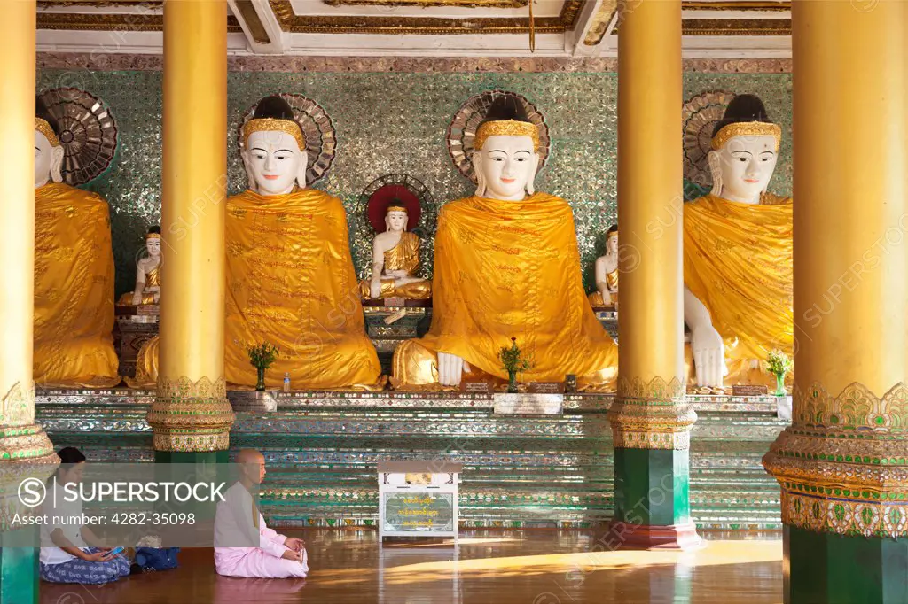 Myanmar, Yangon, Yangon. A nun and woman praying before Buddhas in Shwedagon Pagoda in Yangon Myanmar.