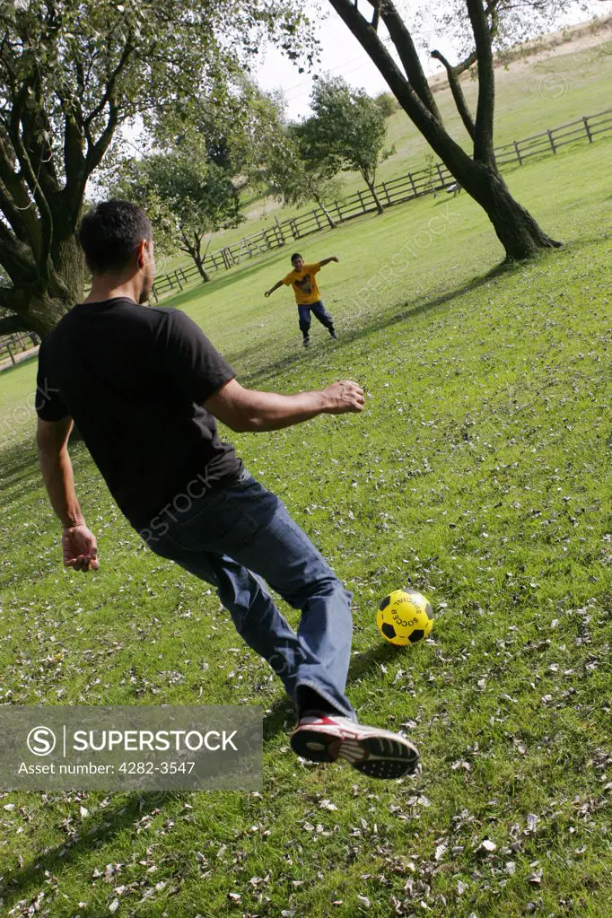 England, Worcestershire, Waseley Hills. Father and son playing football in Waseley Hills Country Park. It is 150 acres of rolling open hills with old hedgerows, pastures and small pockets of woodland with panoramic views.