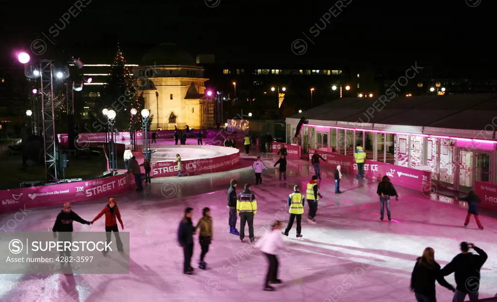 England, West Midlands, Birmingham. Ice skaters in Centenary Square at Christmas time. The glistening 1000m2 outdoor rink in Centenary Square is encircled by twinkling lights and fluttering flags and has become an annual fixture in the city.