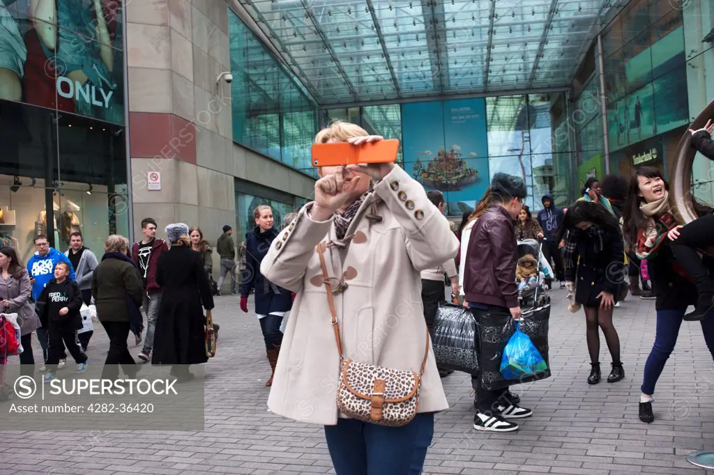 England, West Midlands, Birmingham. A woman taking a photograph with her mobile phone outside the Bullring shopping centre.