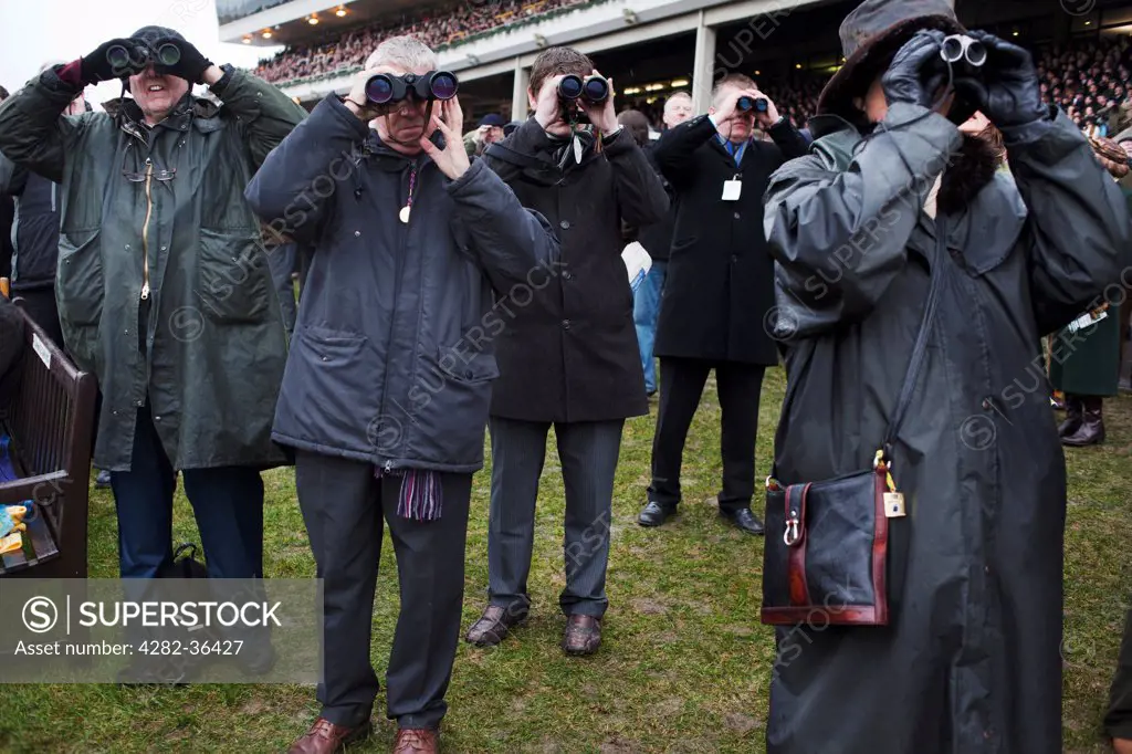 England, Gloucester, Cheltenham. People with binoculars looking at the Gold Cup Day race at the Cheltenham Festival.