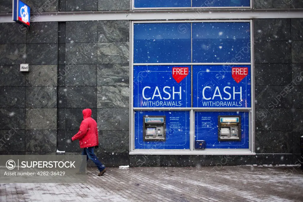 England, West Midlands, Birmingham. A man in a red jacket passes cash machines.