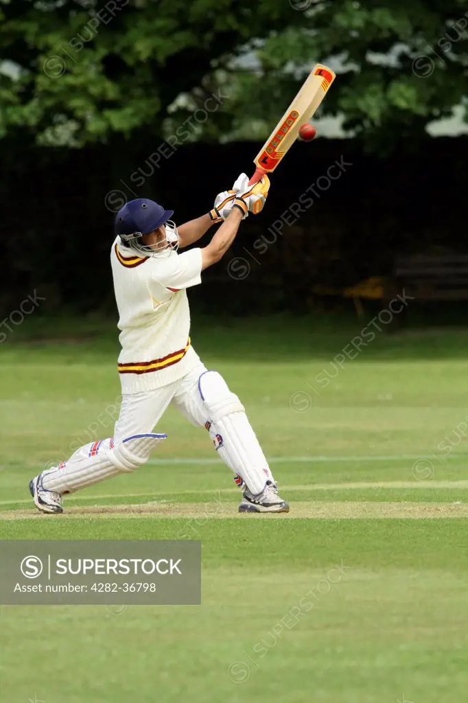 England, West Yorkshire, Bradford. A cricketer in full protective clothing driving the ball towards the viewer.