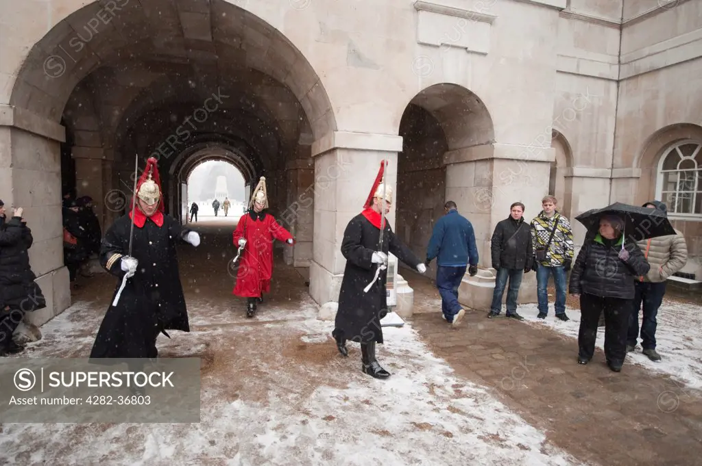England, London, Westminster. Changing of the Guard watched by a handful of tourists in a wintery Horseguards with snowfall at Whitehall.