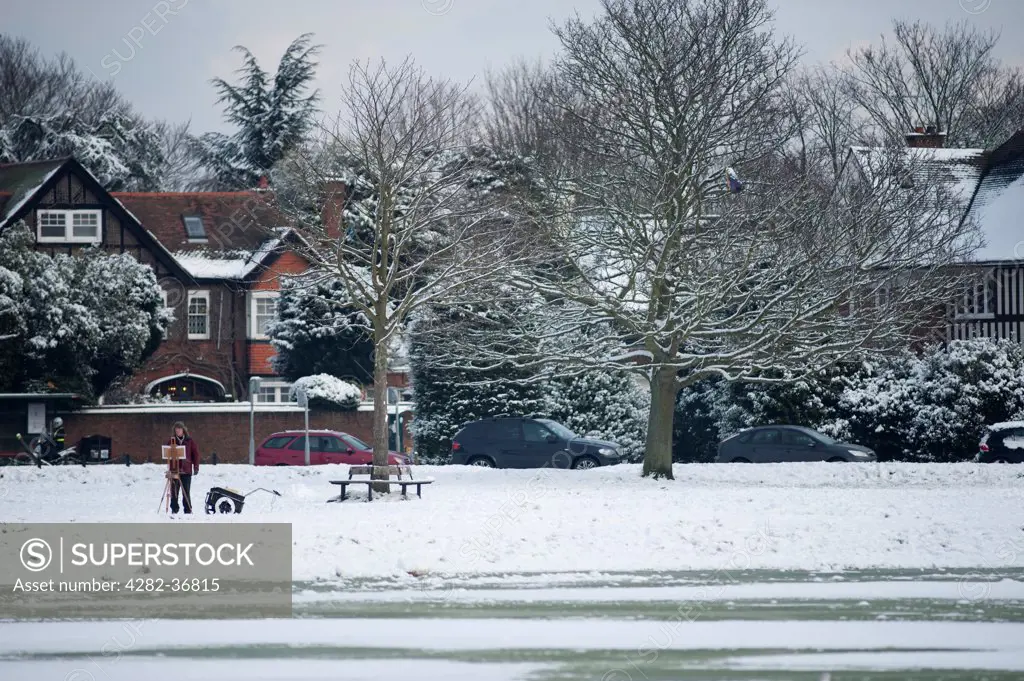 England, London, Wimbledon. Artist sketching on snow covered Wimbledon Common with an ice covered pond in the foreground.