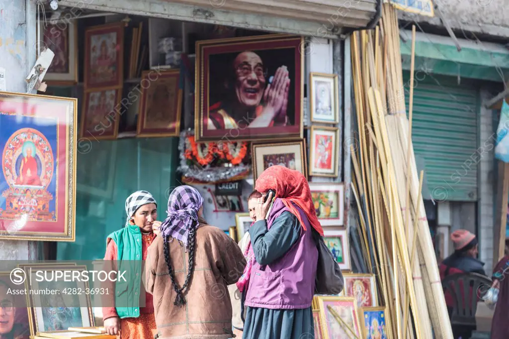 India, Ladakh, Leh. A group of Ladakhi women in front of a printshop with a big portrait of His Holiness Dalai Lama.
