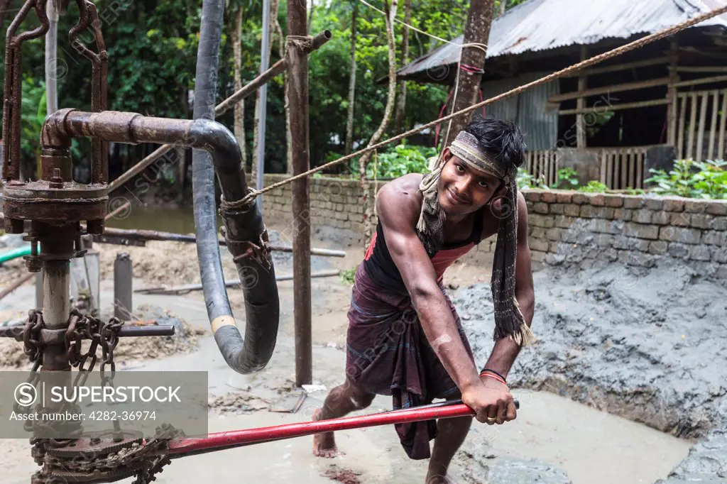 Bangladesh, Barisal, Barisal. A young Bengali man working at an old indigenous water lift and a deep tube well for irrigation of water.