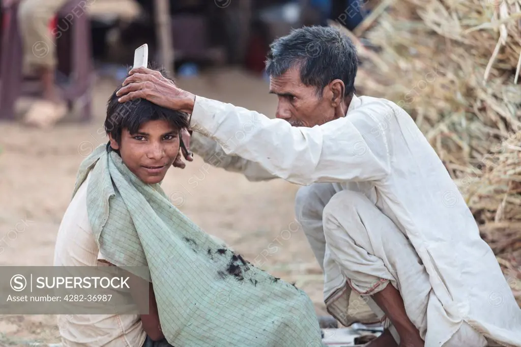 India, Rajasthan, Pushkar. Young boy getting a haircut during the Pushkar Camel Fair.