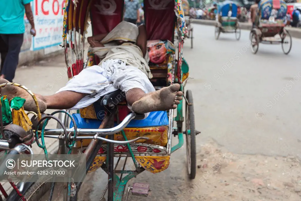 Bangladesh, Dhaka, Dhaka. Man sleeping in his rickshaw on a street.