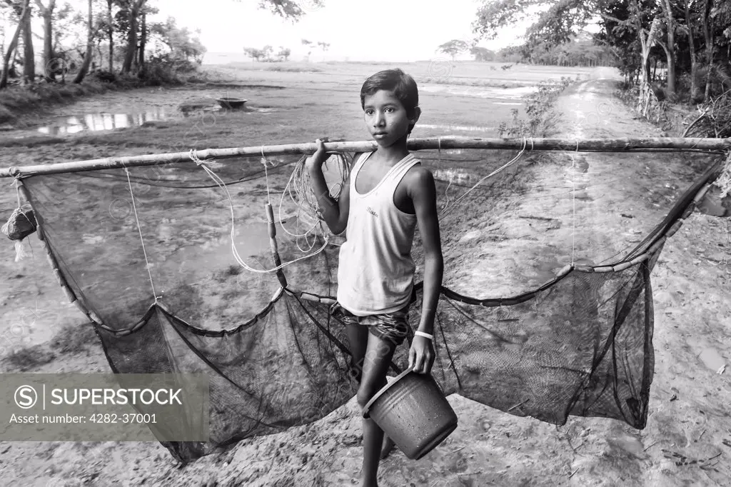 Bangladesh, Barisal, Barisal. Boy with a fishing net and a bucket in his hands on his way to the river.