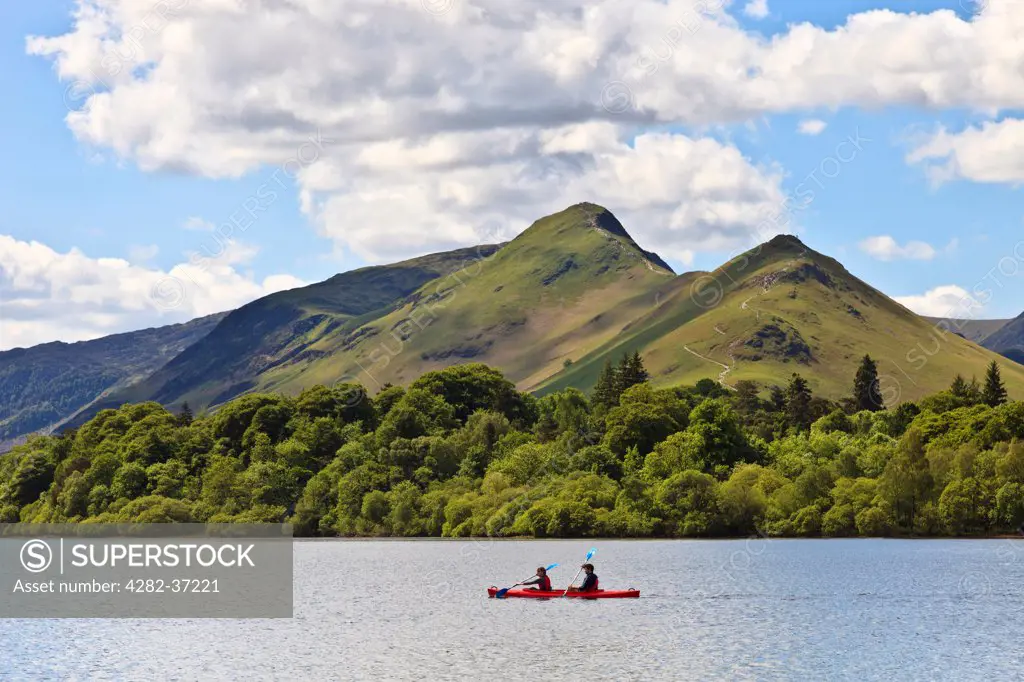 England, Cumbria, Keswick. Two people paddle a red canoe on Derwent Water with Catbells in the background.