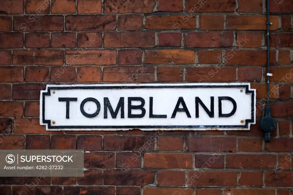 England, Norfolk, Norwich. A sign for the Tombland area of Norwich on a red brick wall.