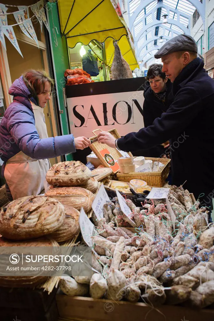 England, London, Brixton. Customers trying samples at a gourmet cheese and sausage shop in Brixton Village.