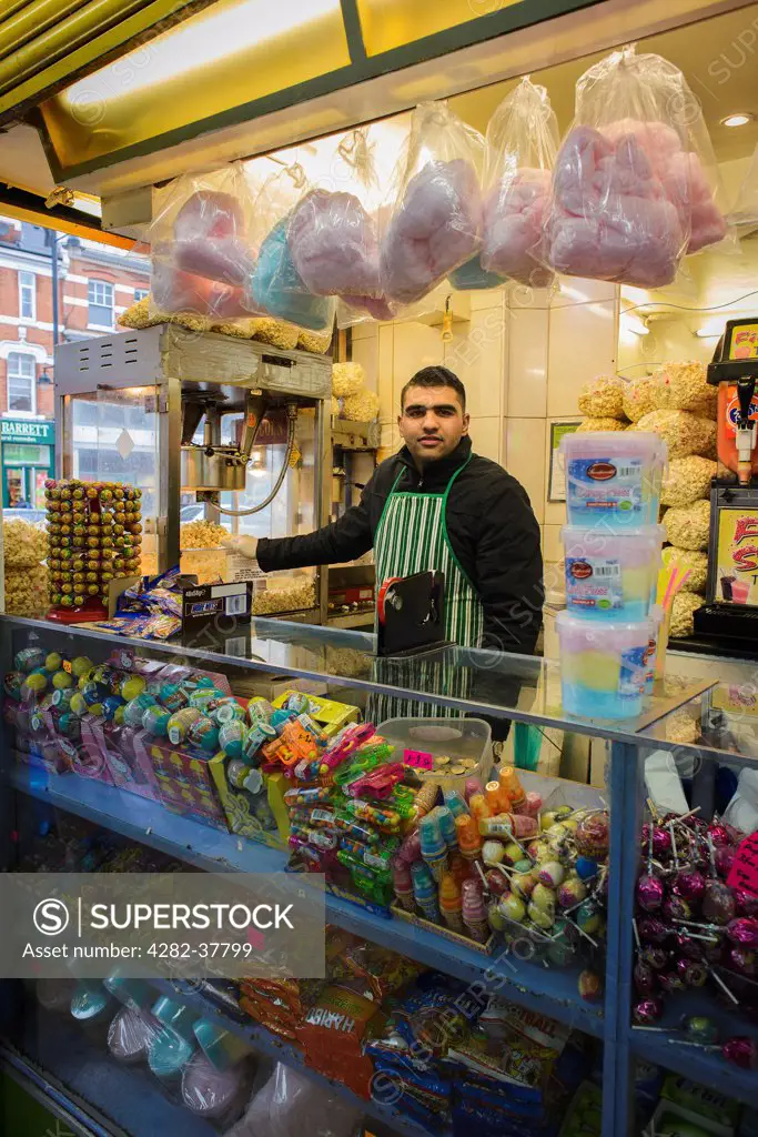 England, London, Brixton. A shopkeeper behind the counter of a sweet shop in Brixton Market.