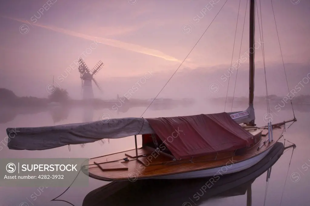 England, Norfolk, Thurne. A misty view across the water to Thurne Mill at sunrise.