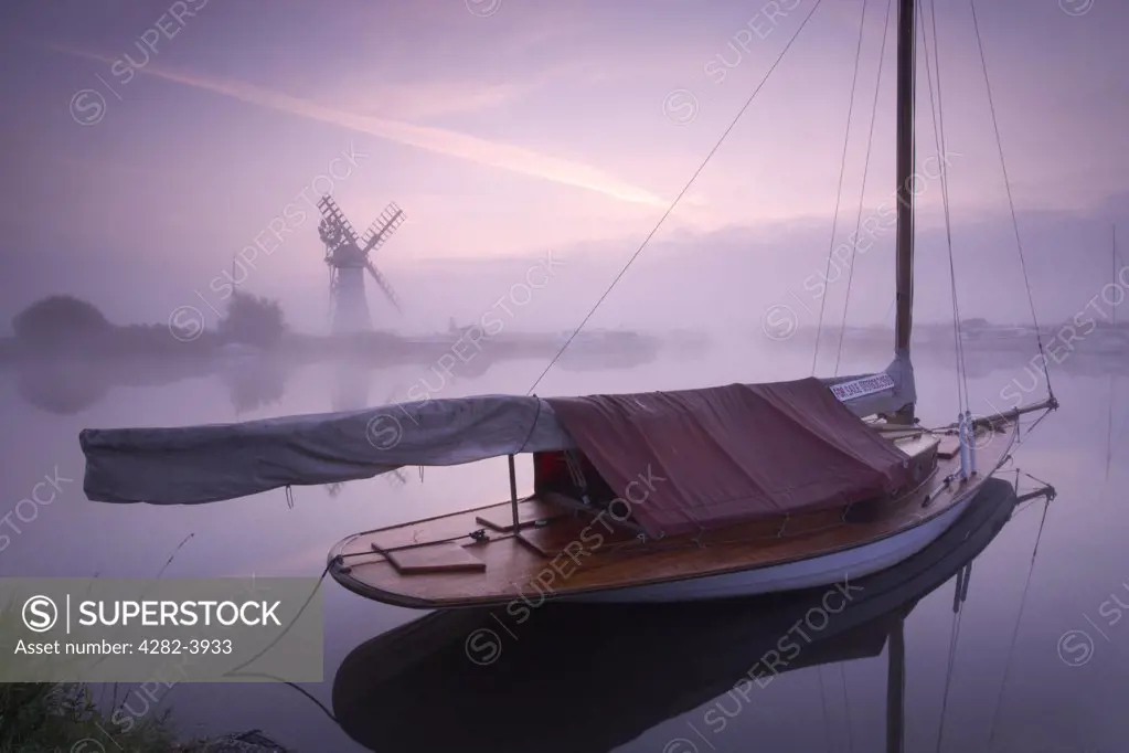 England, Norfolk, Thurne. A misty view across the water to Thurne Mill at sunrise.